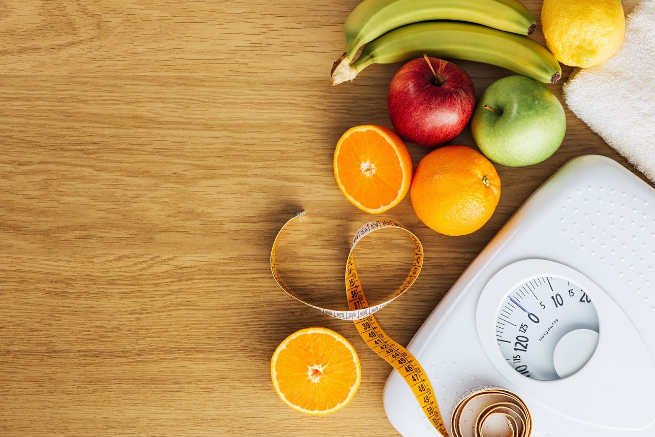 A variety of fresh, colorful fruits and vegetables arranged beside a modern digital scale, symbolizing the balance between healthy eating and weight management.